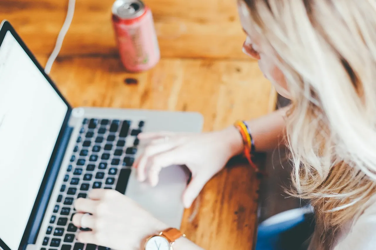Mains sur le clavier d’un ordinateur portable, une boisson à côté